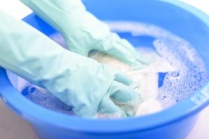 洗面器に衣類を入れて、やさしく押し洗いしている手元の様子。丁寧な手洗いで衣類をいたわる場面