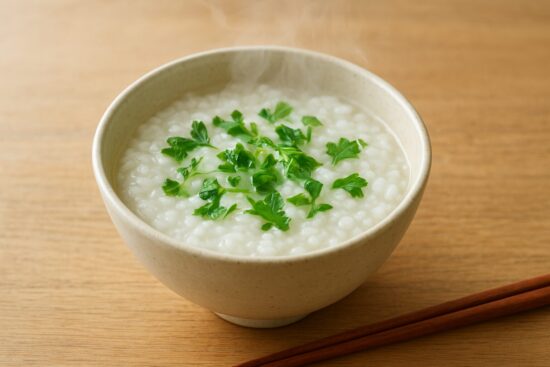 1月7日の行事食「七草がゆ」をテーマにした、やさしくあたたかい雰囲気の和食イメージ。 白いおかゆの中に、緑の七草が彩りよく浮かんでいる様子